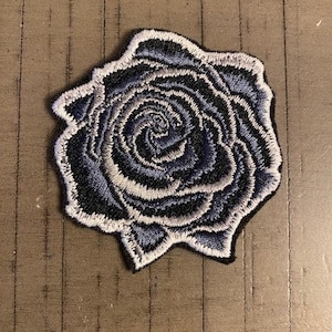May include: A blue and white embroidered rose patch. The rose is a single bloom with a spiral design.