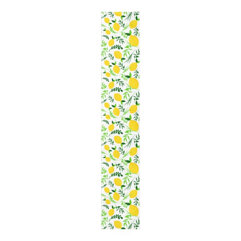May include: A long, rectangular table runner featuring a repeating pattern of bright yellow lemons and vibrant green leafy sprigs set against a crisp white background. The design is evenly distributed across the entire length of the fabric.