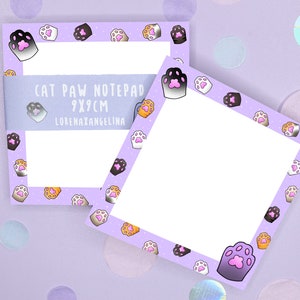 Könnte beinhalten: Zwei lila Notizblöcke mit weißem Hintergrund und einem Rand aus bunten Katzenpfotenabdrücken. Der Notizblock links trägt den Text "CAT PAW NOTEPAD 9X9CM LORENAXANGELINA".