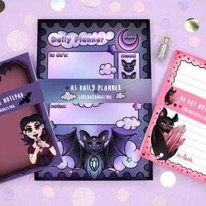 Könnte beinhalten: Drei A6-Notizblöcke mit gotischem Thema. Der erste Notizblock ist lila mit einer Vampir-Illustration und dem Text "A6 Vampire Notepad". Der zweite Notizblock ist lila und blau mit einer Fledermaus-Illustration und dem Text "AS Daily Planner". Der dritte Notizblock ist rosa mit einer Fledermaus-Illustration und dem Text "A6 Bat Notepad".