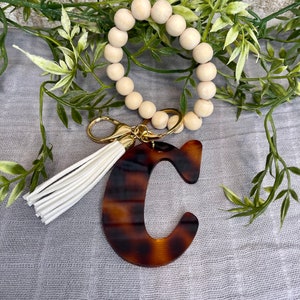 May include: A wooden bead keychain with a white tassel and a brown tortoiseshell letter C charm.