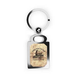 May include: Silver-colored rectangular keychain with a circular key ring. The keychain features a vintage-style illustration of a train and the text "TAKE HIM TO THE TRAIN STATION" on a textured background.