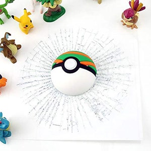 K&ouml;nnte beinhalten: Ein wei&szlig;er Pok&eacute;ball mit gr&uuml;nen und orangen Akzenten, umgeben von einem Effekt aus zerbrochenem Glas. Der Pok&eacute;ball ist ein beliebtes Sammlerst&uuml;ck.