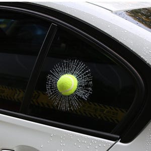 K&ouml;nnte beinhalten: Ein gelber Tennisball scheint ein Autofenster durchbrochen zu haben und einen Risseffekt zu erzeugen. Der Aufkleber ist so konzipiert, dass er wie ein realistisches zerbrochenes Fenster aussieht.