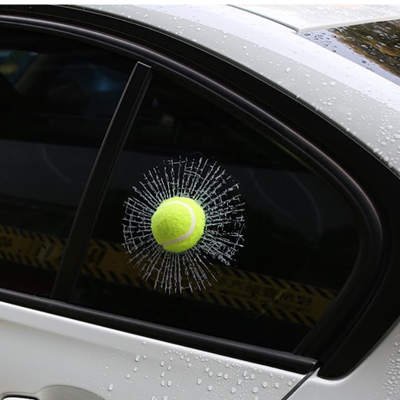 K&ouml;nnte beinhalten: Ein gelber Tennisball scheint ein Autofenster durchbrochen zu haben und einen Risseffekt zu erzeugen. Der Aufkleber ist so konzipiert, dass er wie ein realistisches zerbrochenes Fenster aussieht.