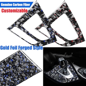Może przedstawiać: Dwa czarne elementy wykończenia wnętrza samochodu z włókna węglowego z czerwono-niebieskim wzorem. Tekst "Genuine Carbon Fiber Customizable" znajduje się w górnej części obrazu. Tekst "Gold Foil Forged Style" znajduje się w dolnej części obrazu. Zbliżenie wnętrza samochodu z czarnym otoczeniem dźwigni zmiany biegów z włókna węglowego z czerwono-niebieskim wzorem.