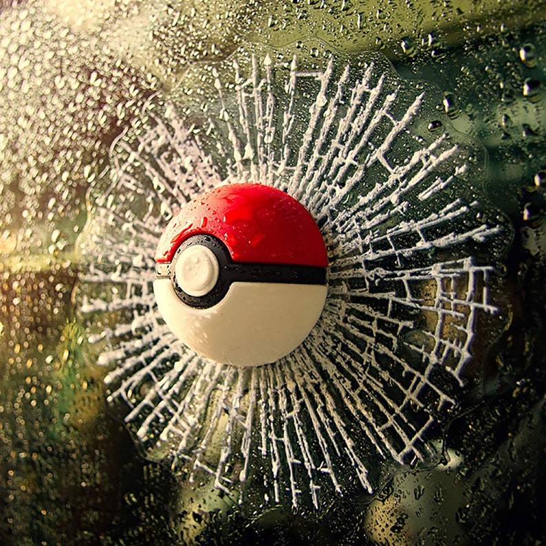 K&ouml;nnte beinhalten: Ein roter und wei&szlig;er Poke Ball Aufkleber mit einem Risseffekt aus Glas. Der Aufkleber ist so konzipiert, dass er wie ein zerbrochenes Fenster mit Glassplittern aussieht, die vom Zentrum nach au&szlig;en strahlen.