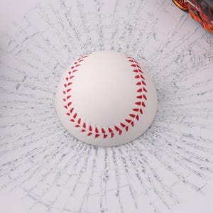 K&ouml;nnte beinhalten: Ein wei&szlig;er Baseball mit roten N&auml;hten wird vor einem Hintergrund aus zerbrochenem Glas gezeigt. Der Effekt des zerbrochenen Glases ist ein Aufkleber.