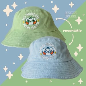 May include: Reversible bucket hat with two different embroidered designs. One side features a green hat with a white cartoon bear with the text "No Thoughts Head Empty". The other side features a blue hat with a white cartoon bear with the text "Many Thoughts Head Full".