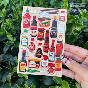 May include: A sticker sheet featuring illustrations of various Asian cooking sauces and ingredients. The sheet includes images of sriracha, soy sauce, sesame oil, rice vinegar, and more. The text "Drawn By Ivy" is visible.