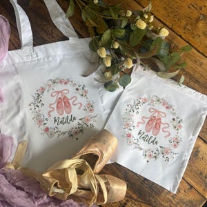 May include: White tote bag and drawstring bag featuring a floral wreath design and ballet shoes. The name "Matilda" is printed in cursive. Ballet pointe shoes with ribbons are in the foreground.
