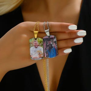 Könnte beinhalten: Zwei personalisierte Halsketten mit Hundemarken. Eine hat eine goldene Kette und ein Foto eines Mannes, der ein kleines Tier hält. Die andere hat eine silberne Kette und ein Foto einer Person in einer blauen Jacke. Beide Anhänger sind rechteckig.