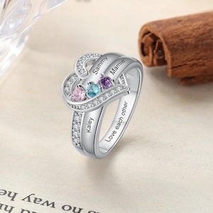 Peut inclure: Bague en argent en forme de cœur avec trois pierres précieuses colorées et les mots "Sammy", "Mamie", "Kaley" et "Love each other" gravés sur la bande.