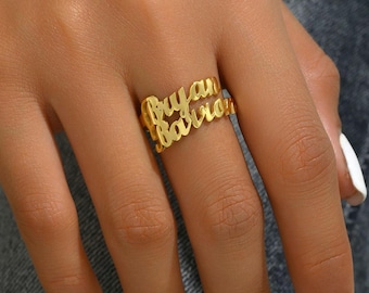 May include: A gold-colored ring with the names "Bryan" and "Barron" in a cursive font. The ring is worn on a finger, showcasing the personalized design. The ring is a piece of jewelry.