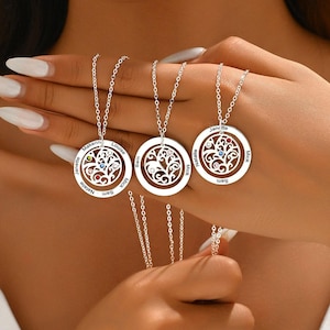 Peut inclure: Trois colliers pendentifs argentés avec des pendentifs circulaires. Chaque pendentif présente un motif d'arbre de vie avec des pierres précieuses colorées et des noms personnalisés. Les colliers sont présentés sur une main.