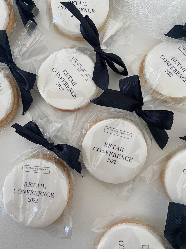 May include: White round cookies with black ribbon bows. Each cookie is decorated with the text "The White Company" and "Retail Conference 2022".