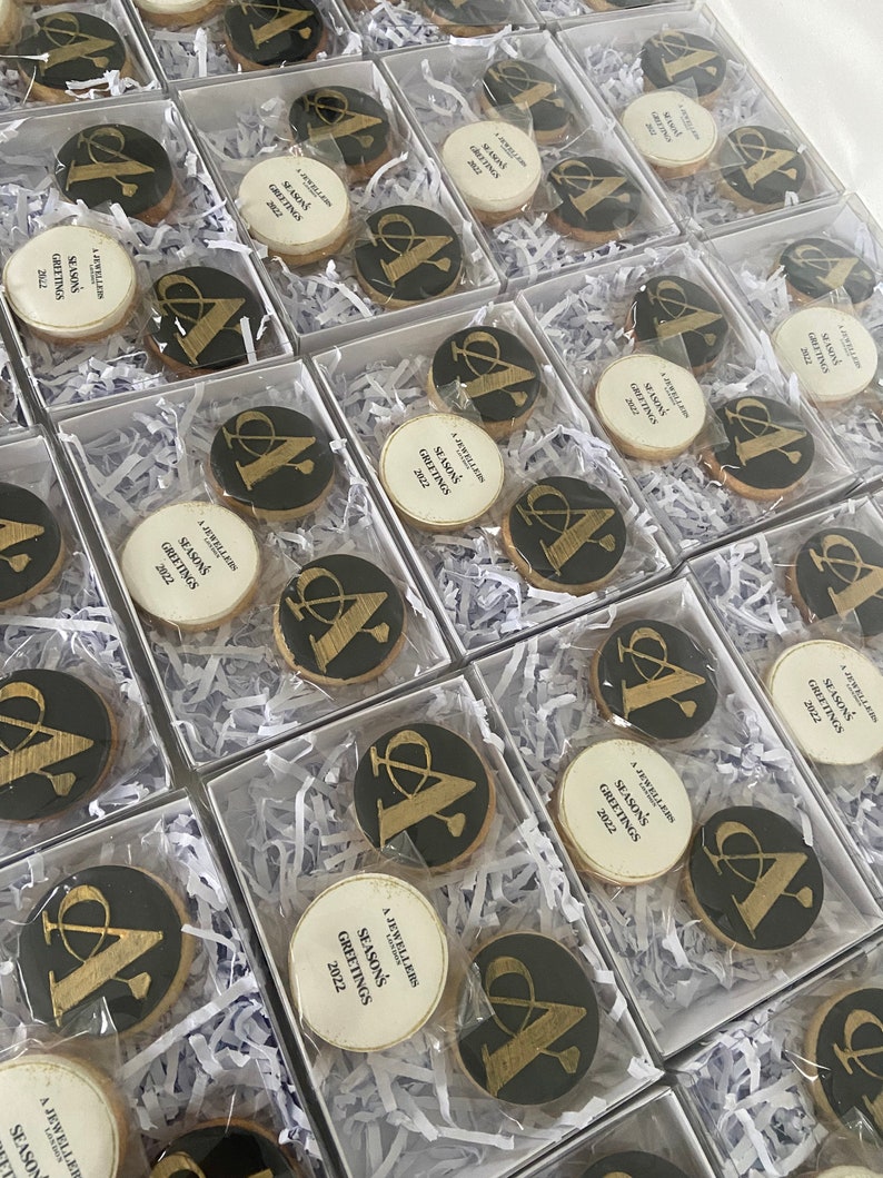 May include: A collection of small, white boxes filled with black and gold cookies. Each cookie has a gold letter "A" and the text "A Jewellers London Season's Greetings 2022".