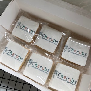 May include: A white box with six individually wrapped cookies. Each cookie is decorated with a logo that says "Cherubs Montessori Day Nursery".