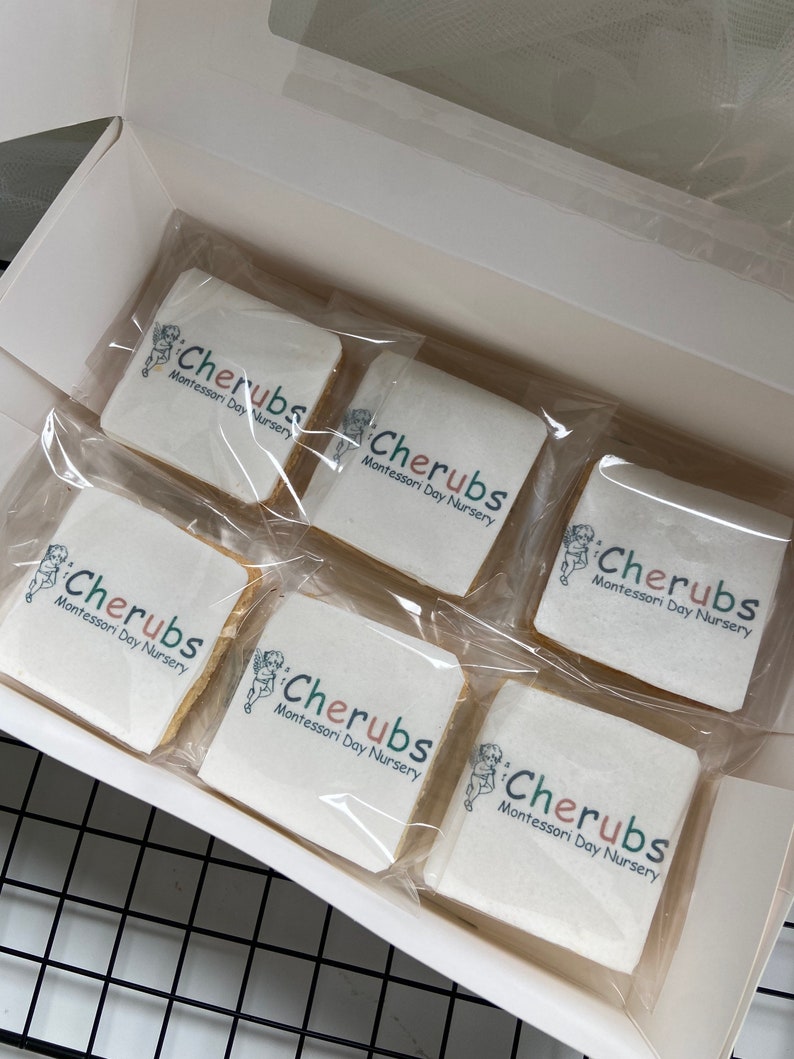 May include: A white box with six individually wrapped cookies. Each cookie is decorated with a logo that says "Cherubs Montessori Day Nursery".