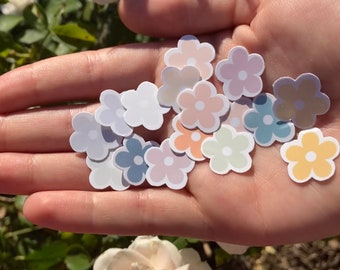 May include: A collection of pastel colored flower stickers in various shades of pink, blue, yellow, and green. The stickers are in the shape of a simple flower with five petals.