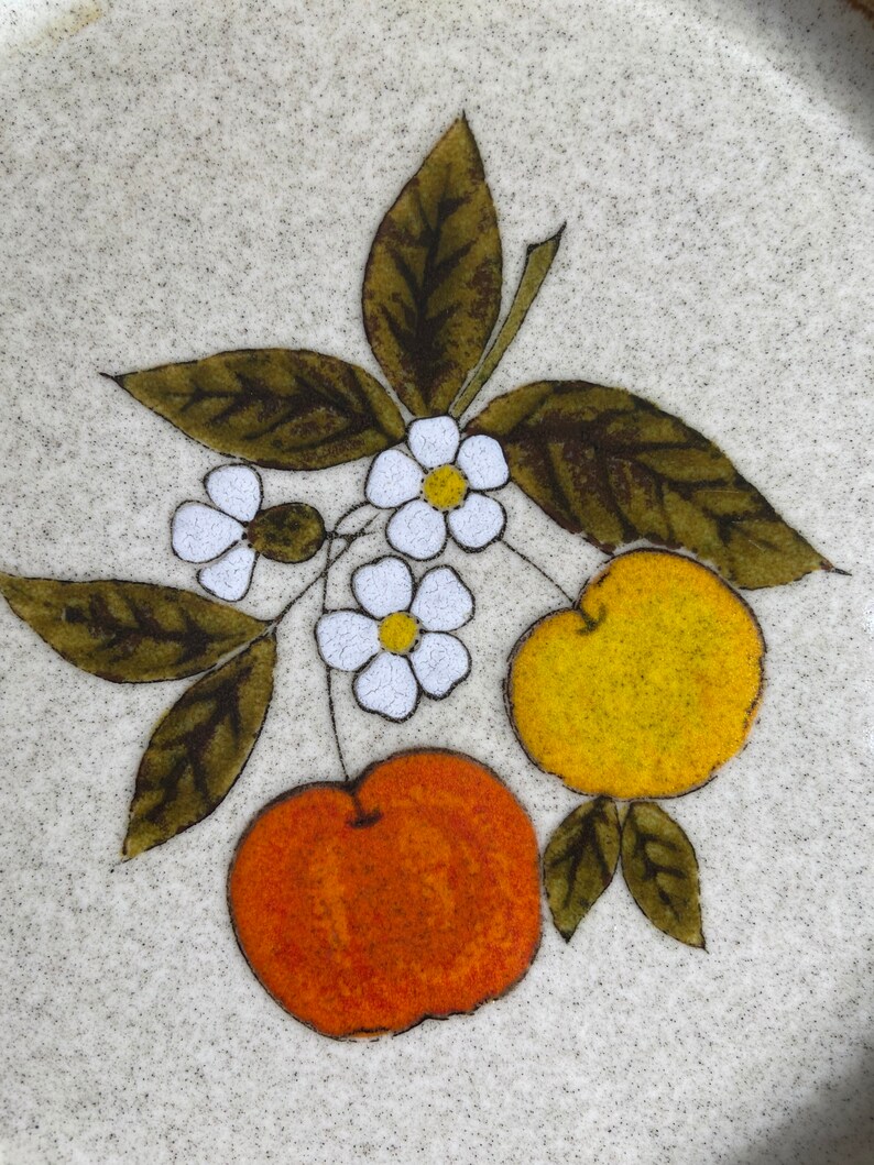 Pode incluir: Um prato de cer&acirc;mica com fundo branco e um desenho floral castanho, verde e amarelo. O desenho apresenta duas cerejas laranja e amarelas e flores brancas com centros amarelos.
