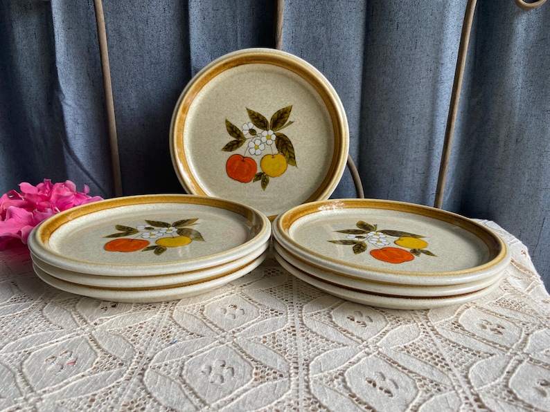 Pode incluir: Conjunto de quatro pratos de jantar de cer&acirc;mica marrom e branco com um design de frutas c&iacute;tricas. Os pratos t&ecirc;m uma borda marrom e um centro branco com um ramo de c&iacute;tricos marrom com frutas laranja e amarelas e flores brancas.