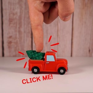 May include: A red toy pickup truck with a green Christmas tree in the bed. The text "CLICK ME!" is displayed below the truck. A finger is pointing at the tree. The truck has black wheels and a blue window.