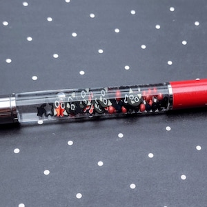 May include: A red and clear pen with black and red glitter inside. The pen has a silver cap.