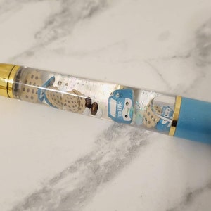 May include: A blue and gold pen with a clear section filled with glitter, small cookies, and a blue milk carton charm.
