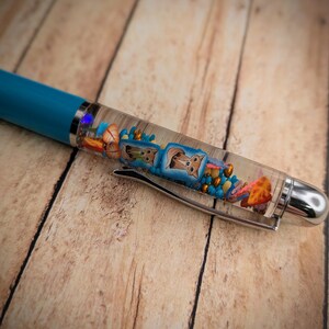 May include: A turquoise blue pen with a clear barrel filled with colorful beads, small animal figurines, and glitter.