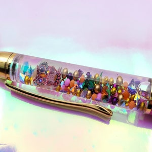 May include: A pink pen with a clear section filled with colorful glitter and beads. The pen has a gold-colored cap and trim.