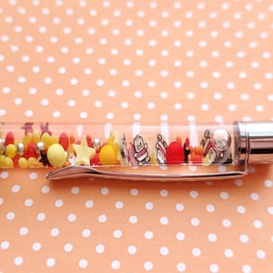 May include: A red and clear pen with a silver clip. The clear portion of the pen is filled with colorful beads and small figurines.
