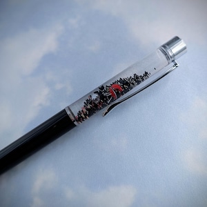 May include: A black and silver pen with a clear section filled with black and red glitter. The glitter is swirling inside the pen.