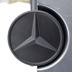 May include: A close-up of a black Mercedes-Benz logo on a silver car.