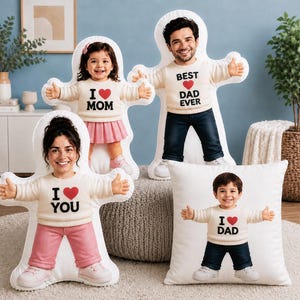 May include: Four custom-shaped pillows featuring photographic prints of people. Three pillows are die-cut in the shape of a person with arms outstretched, wearing cream sweaters with red hearts and text reading I LOVE MOM, BEST DAD EVER, and I LOVE YOU.