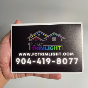 May include: A black rectangular card with the text "1st Coast Trimlight" and a website address and phone number. The logo features a house silhouette with a rainbow-colored roof.