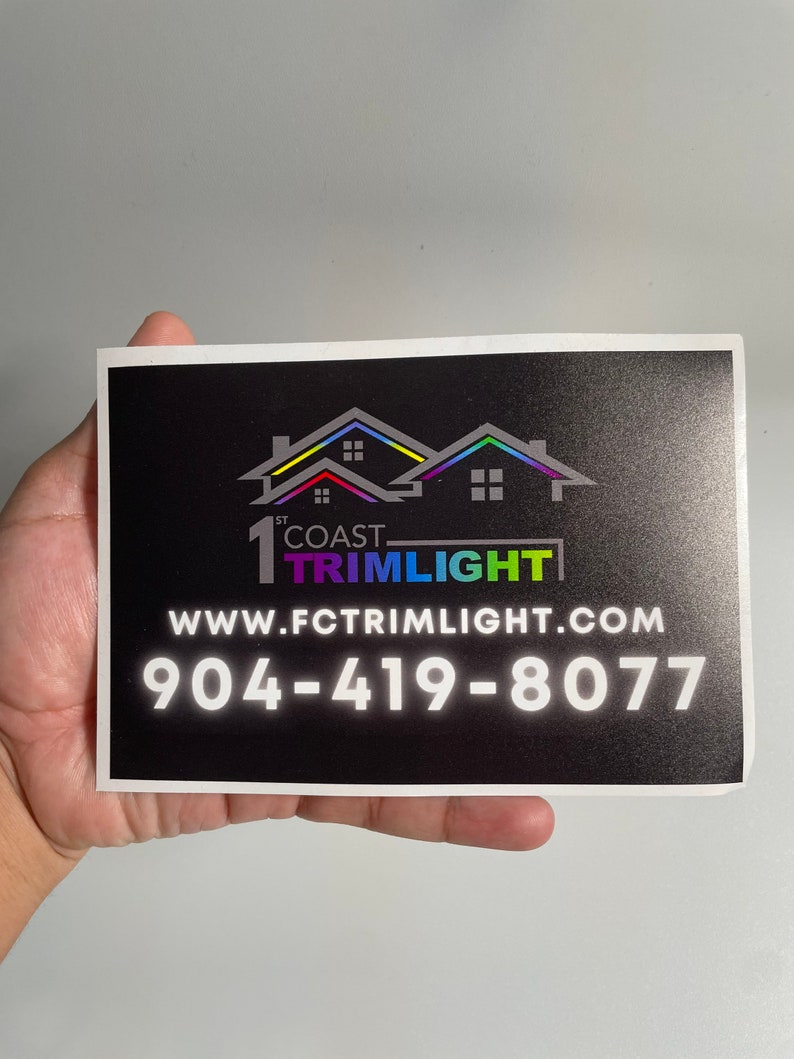May include: A black rectangular card with the text "1st Coast Trimlight" and a website address and phone number. The logo features a house silhouette with a rainbow-colored roof.