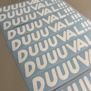May include: A stack of white stickers with the word "DUUUVAL!!!" printed in a bold, rounded font. The stickers are on a light blue backing, and the text is centered on each sticker.
