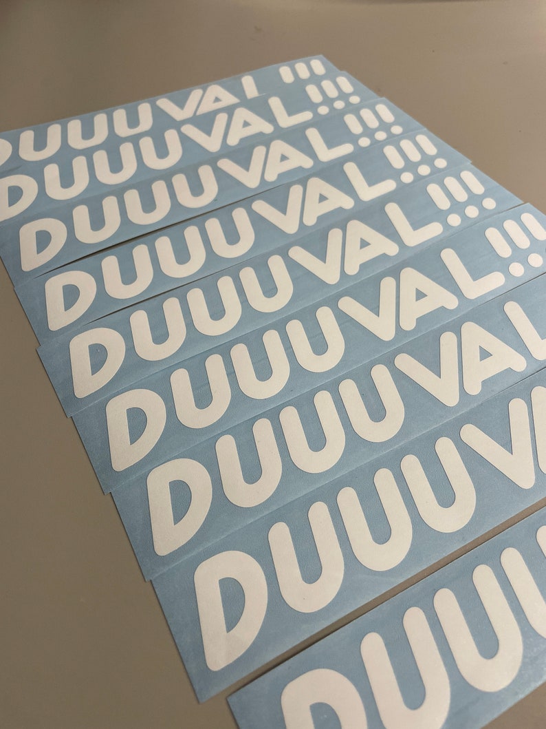 May include: A stack of white stickers with the word "DUUUVAL!!!" printed in a bold, rounded font. The stickers are on a light blue backing, and the text is centered on each sticker.