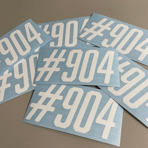 May include: A collection of white vinyl stickers with the text "#904" printed on them. The stickers are rectangular with rounded corners and are arranged on a light blue background.