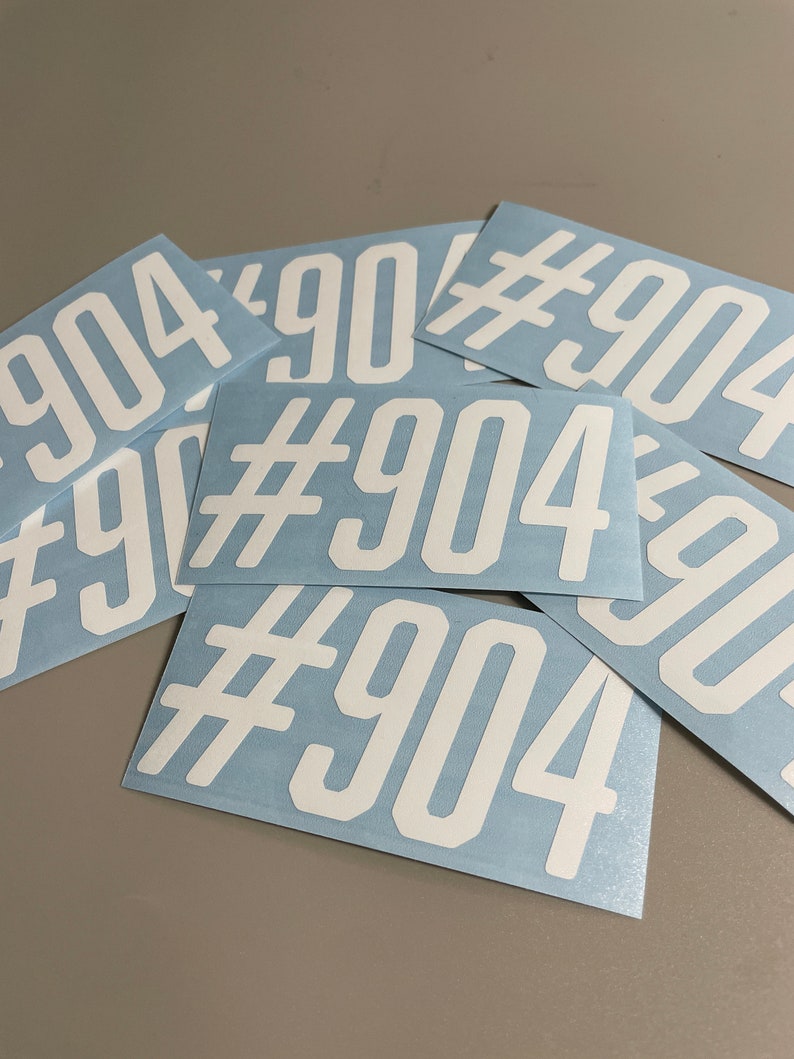 May include: A collection of white vinyl stickers with the text "#904" printed on them. The stickers are rectangular with rounded corners and are arranged on a light blue background.