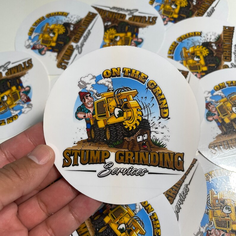 May include: Round sticker featuring a cartoon illustration of a yellow stump grinder with the text "ON THE GRIND" and "STUMP GRINDING Services". The design includes a worker and a surprised-looking tree stump.