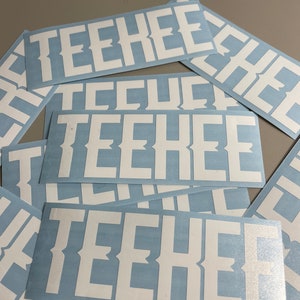 May include: A collection of rectangular stickers with the word "TEEHEE" in bold, white, serif font. The stickers have a light blue background. The stickers are scattered across a surface.