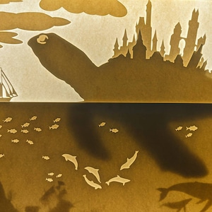 May include: A silhouette of a city on a turtle's back, with a sailboat in the water below. The turtle's shadow is cast on the water, with fish and dolphins swimming around it.