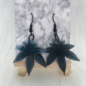 Op de afbeelding: Een paar oorhangers met een donkerblauw glitterbladontwerp met zwarte haken.