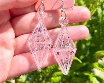 May include: A pair of pink glitter diamond-shaped earrings with silver hooks.