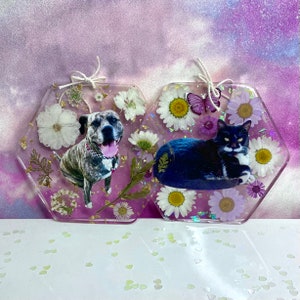 May include: Two hexagonal resin ornaments with pressed flowers and gold leaf. One features a black and white cat, the other a brindle dog.