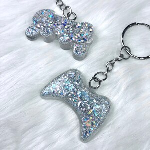 May include: Two silver glitter resin keychains. One is a video game controller and the other is a cloud shape.