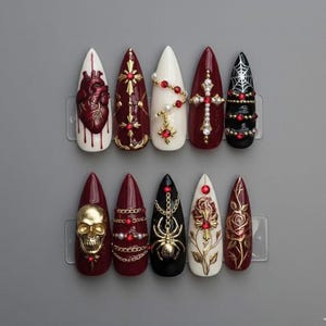 May include: A collection of ten long, pointed artificial nails. Designs include a gold skull, a spider, a heart, crosses, and roses. Colours are white, black, and burgundy, with gold and red accents. Each nail is mounted on a clear plastic holder.