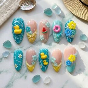 May include: A set of ten almond-shaped artificial nails with summer-themed designs. The nails feature various designs, including a yellow rubber duck, watermelon slices, and floral accents. Colors include blue, pink, yellow, and white.